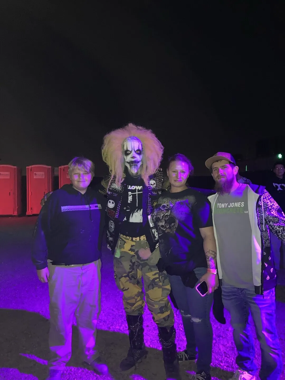Four guests pose with a wild-haired clown character under purple light