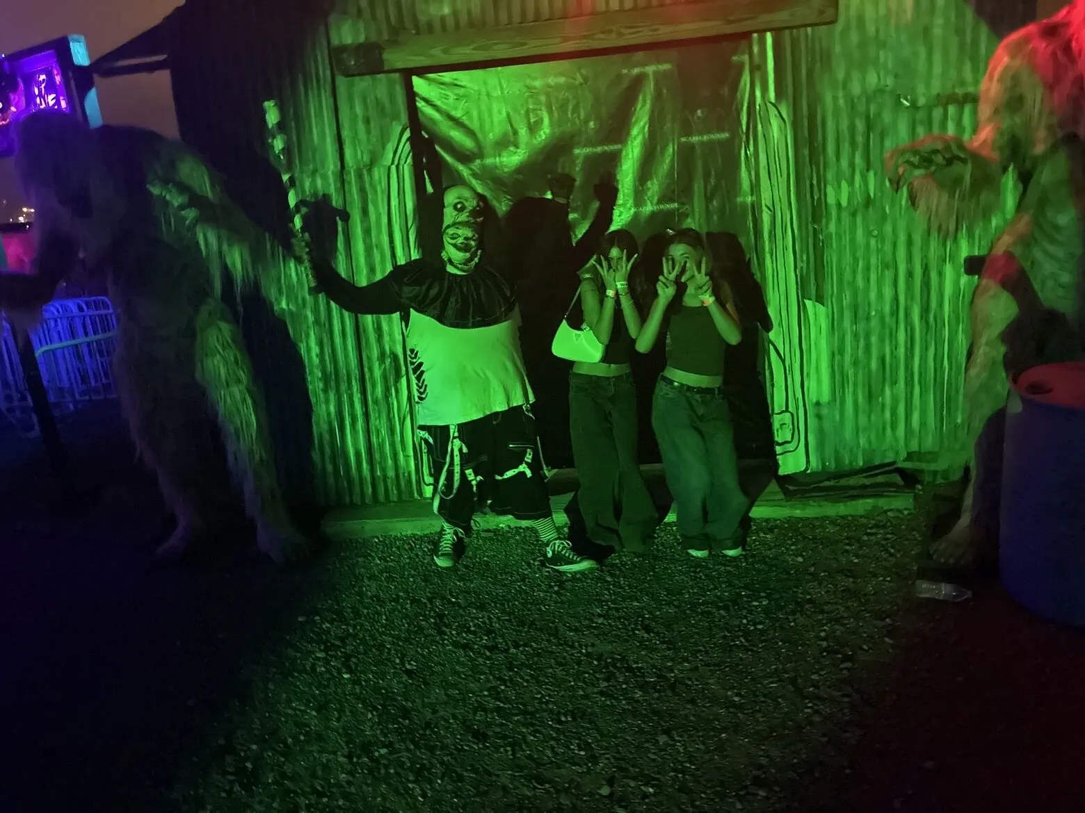 Guests cover their eyes as creatures close in outside a green-lit haunted house front