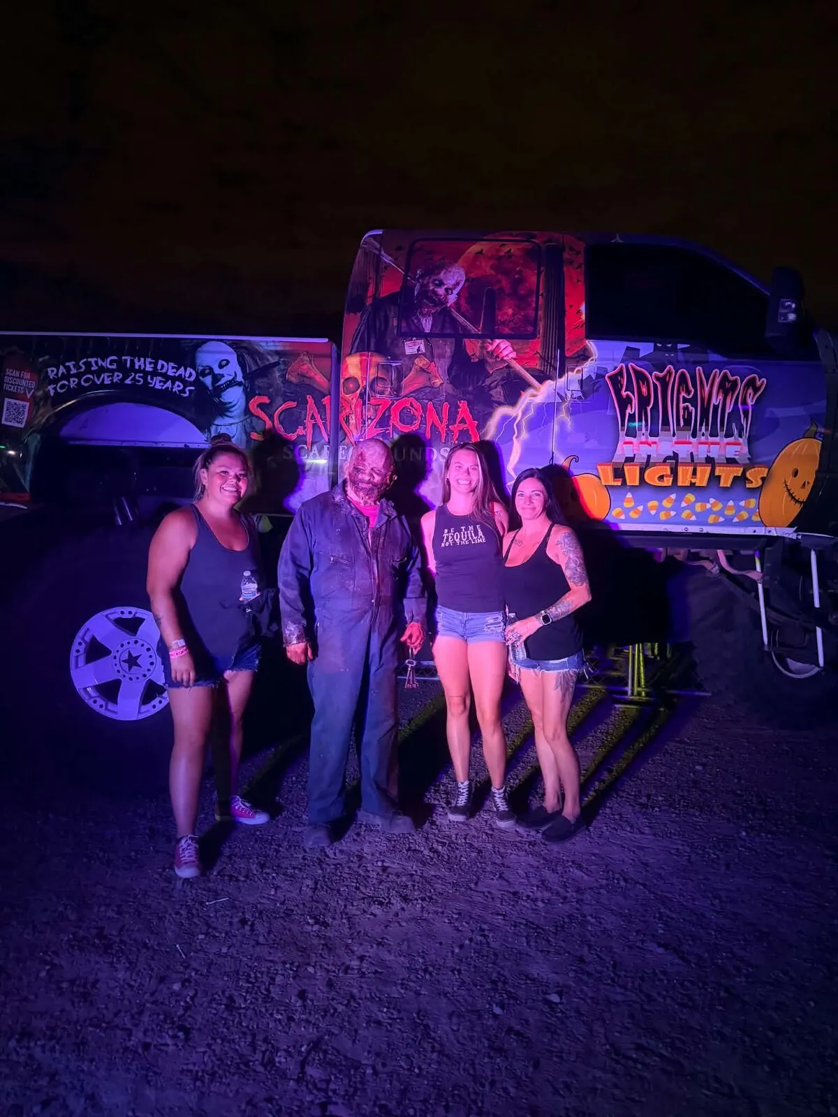 Three guests pose with a character in coveralls beside the painted Scarizona truck