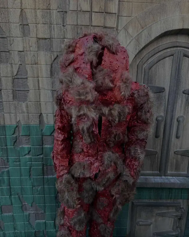 A blood-red flayed-creature character standing head bowed on the Scarizona Scaregrounds set