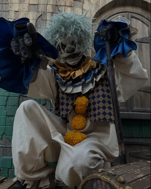 A Scarizona pierrot-clown scare actor seated with a cane at the scaregrounds facade