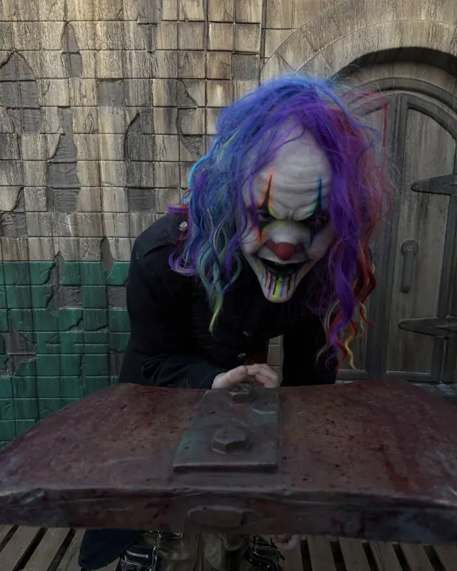 A rainbow-haired clown scare actor leaning over a blood-stained table on the Scarizona set