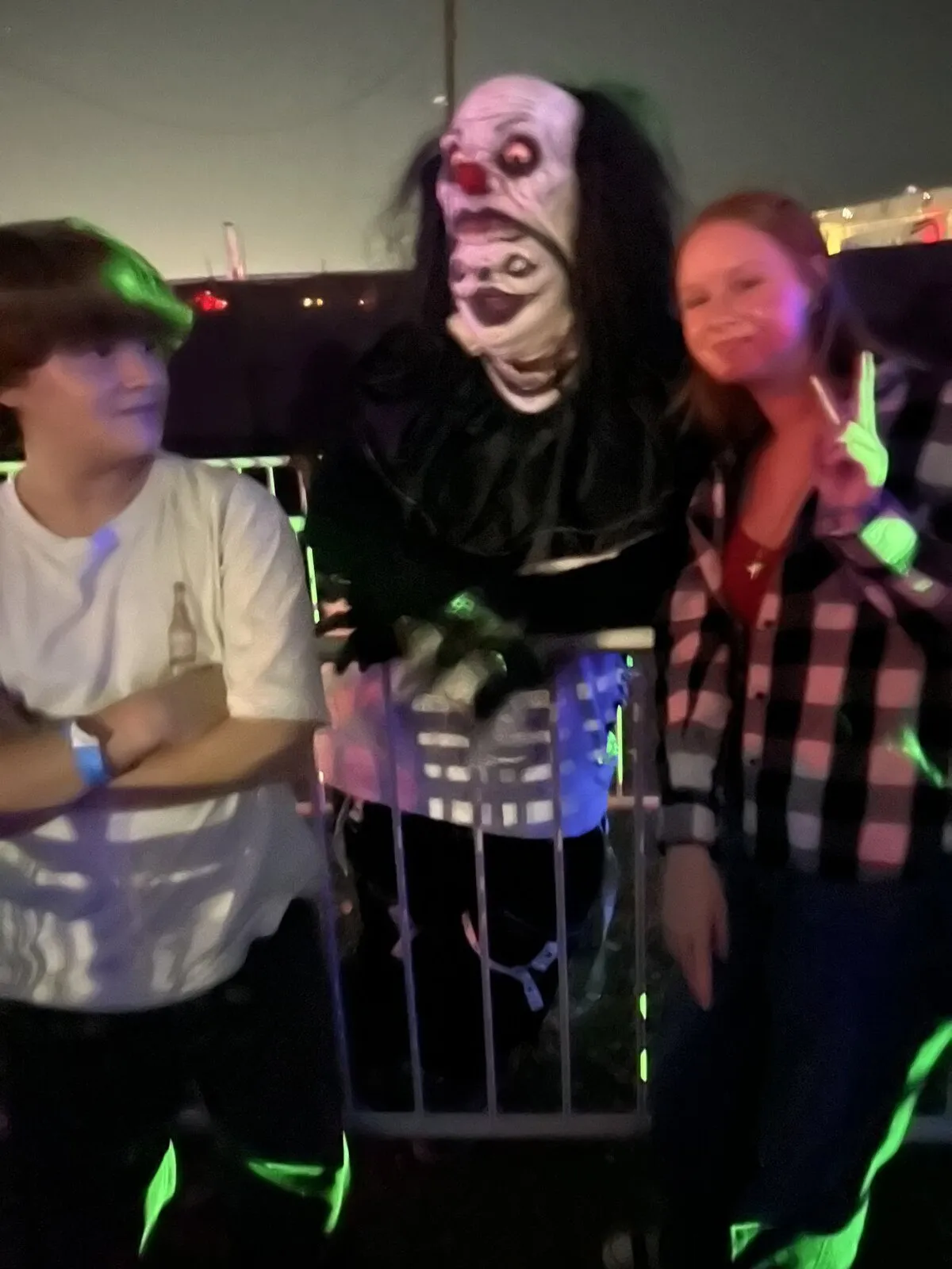 Two young guests pose with a pale-faced clown character at night